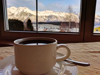 Cup of coffee on the table. seen through window  snow covered mountain range the austrian alps.