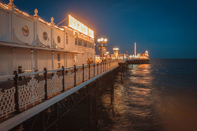 Illuminated bridge over sea against sky at night