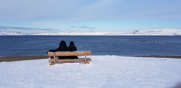 Rear view of couple sitting on beach against sky