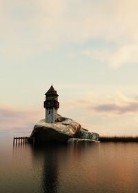 Tower on rock in sea against cloudy sky during sunset