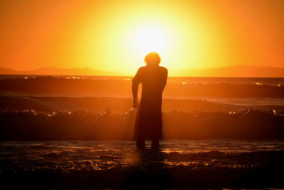 Silhouette man standing by sea against sky during sunset