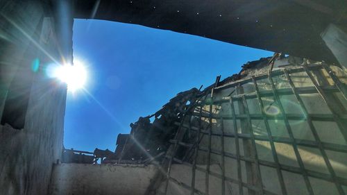 Low angle view of sunlight streaming through buildings against sky