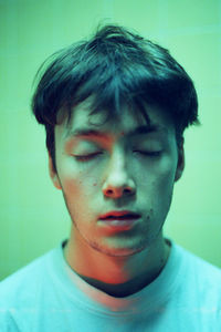 Close-up of young man with eyes closed standing by wall