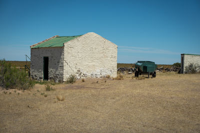 Abandoned house on field against clear blue sky