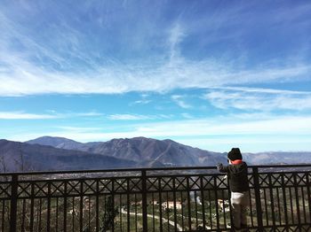 Rear view of woman standing on railing against mountains