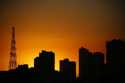 Silhouette buildings and tower in against orange sky at sunset