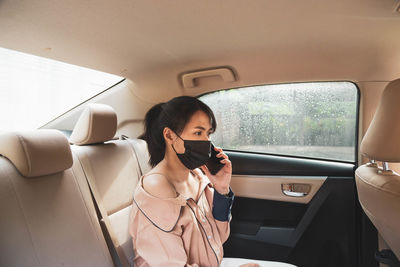 Side view of woman wearing mask talking on phone while sitting in car