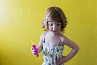 Cute girl holding toy against yellow wall