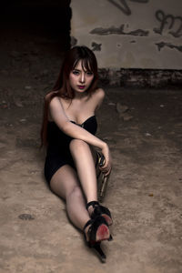 Portrait of beautiful woman holding handgun while sitting on floor in abandoned room