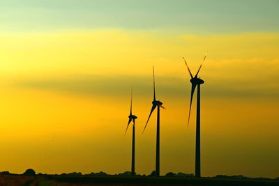 Silhouette wind turbines on field against sky during sunset