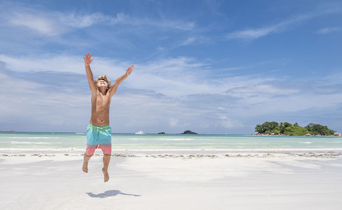 Young boy jumping of joy on tropical beach, summer holiday concept