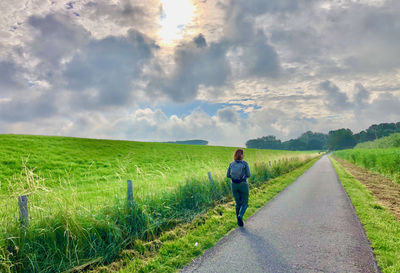 Rear view of woman walking on a road in rural landscape under a clouded sun
