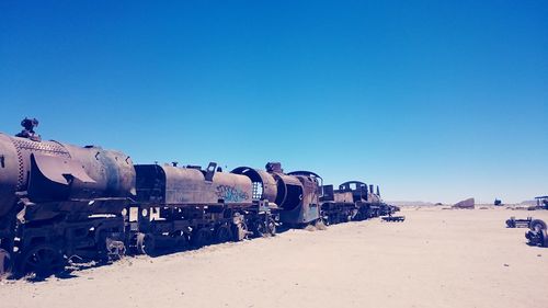 Abandoned train on desert against clear blue sky