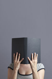 Midsection of woman reading book against gray background