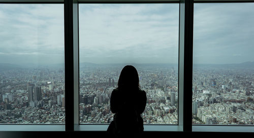 Rear view silhouette woman looking through window