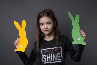 Portrait of smiling girl holding paper eater bunny against gray background