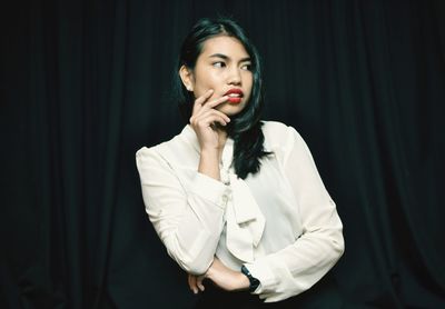 Young woman looking away while standing against black background