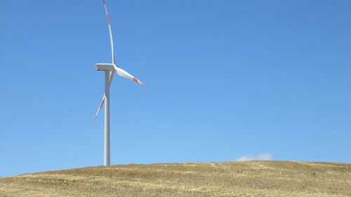 Low angle view of windmill on field against clear blue sky