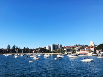 Boats in sea by buildings against clear blue sky