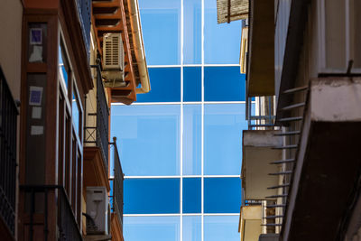 Bright glass facade of a new building reflecting the blue sky, seen from a dark alley