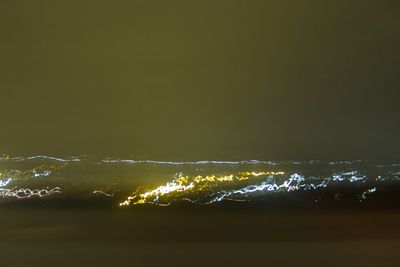 Illuminated city by sea against sky at night