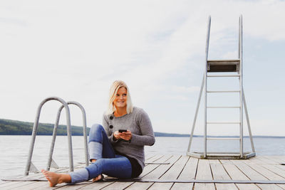 Full length of woman sitting on ladder at shore