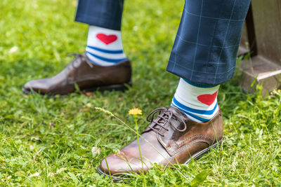 A detail on a groom's shoes and socks with red heart decotarion, sitting in a garden on a sunny day 