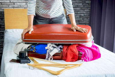 Woman packing suitcase while sitting on bed at home