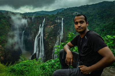 Young man sitting against waterfall