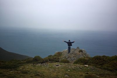 Rear view of man standing on mountain by sea against sky