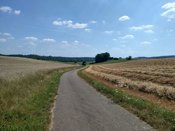 Empty road amidst field against sky