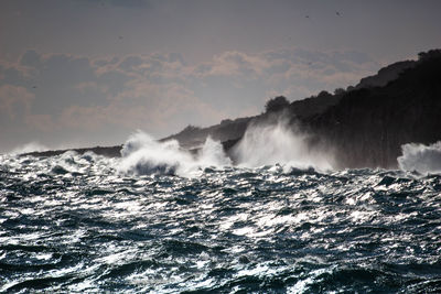 Scenic view of sea waves splashing against sky