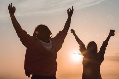 Rear view of woman with arms raised standing against sky during sunset