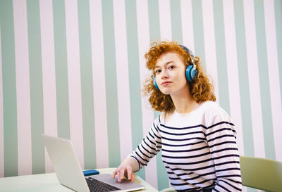 Young woman with laptop listening music through headphones in cafe