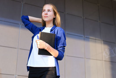 Portrait of young woman standing against wall