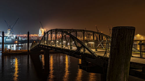 Illuminated bridge over river against sky at sunset