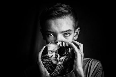 Portrait of young man holding camera over black background