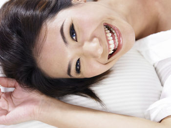 Close-up portrait of smiling woman lying down on bed at home