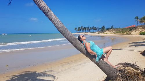 Woman relaxing on beach against blue sky