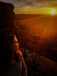 Thoughtful woman looking away while sitting on mountain against sky during sunset
