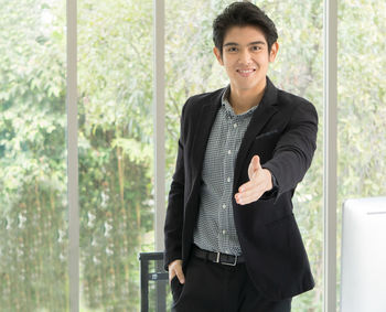 Portrait of young man standing against window