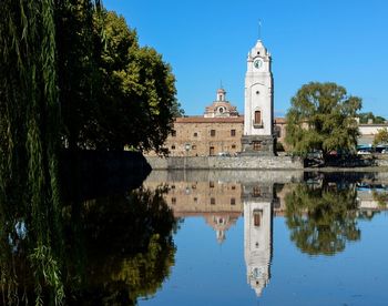 Reflection of trees in lake by building against sky