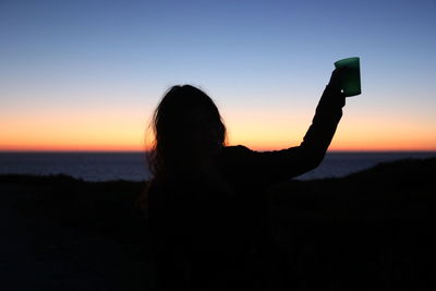 Silhouette woman raising toast against blue sky during sunset