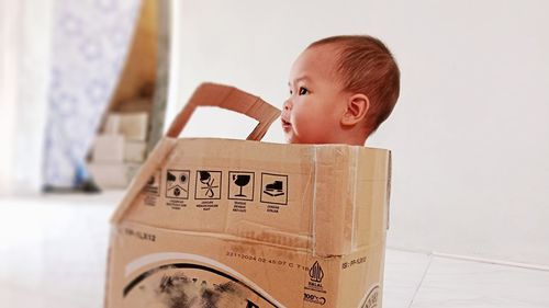 A baby boy is playing in a toy car made from cardboard used for shipping packages