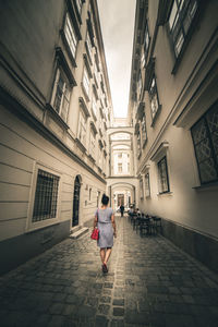 Rear view of woman walking on footpath amidst buildings