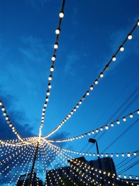 Low angle view of illuminated light bulbs against blue sky