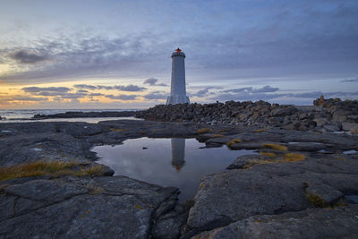 Lighthouse amidst sea and buildings against sky