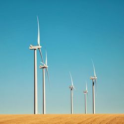 Low angle view of windmills on field against clear blue sky