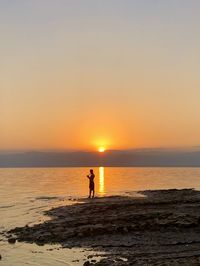 Silhouette woman standing at beach against sky during sunset