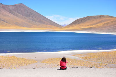 Rear view of woman on beach against mountain